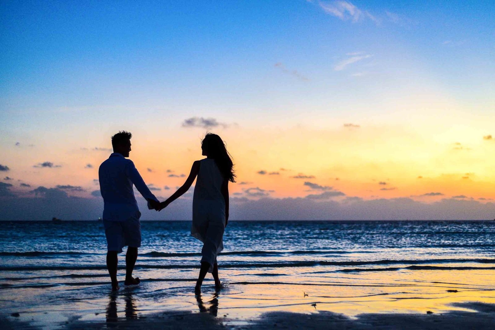 A couple holding hands at the water’s edge at sunset